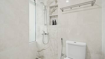 Un baño moderno con ducha, inodoro y un estante con artículos de aseo.
