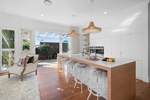 A modern kitchen with a central island, bar stools, and a dining area with a chair and a table.