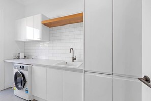 A modern kitchen with white cabinetry, a built-in washing machine, and a wooden beam ceiling. - Luxury On Lemon (New Plymouth)