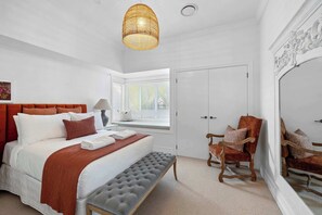 A bedroom with a bed, a bench, a chair, a lamp, and a window with blinds. - Luxury On Lemon (New Plymouth)