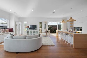 A modern living room with a white sofa, a television, and a dining area with bar stools. - Luxury On Lemon (New Plymouth)