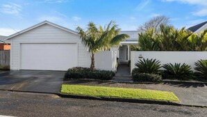 A residential property with a garage, a covered entryway, and a well-maintained front yard with palm trees and shrubs. - Luxury On Lemon (New Plymouth)