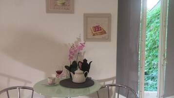 Un coin repas avec une table, des chaises, une théière, une tasse et un verre de vin rouge. Deux tableaux encadrés sont accrochés au mur.