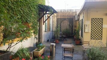 Une cour extérieure agrémentée de plantes en pot, d’un banc en métal et de l’entrée d’un bâtiment.