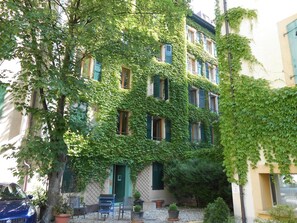 En byggnad med en grön fasad täckt av murgröna, flera fönster och en dörr.