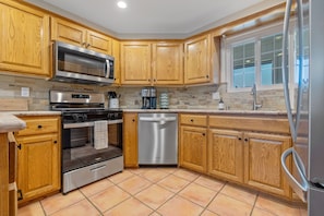 A kitchen with wooden cabinets, a stainless steel refrigerator, a dishwasher, and a microwave. - Sandpiper Dune Escape - Steps to the Beach & Dunes - 5 Bedrooms (Oceano)