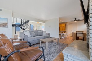 Un salon moderne avec un canapé en cuir, un divan gris, une table basse et un escalier menant à un niveau supérieur.
