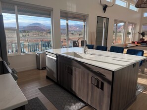 Une cuisine moderne dotée d’un grand îlot central, d’appareils électroménagers intégrés et offrant une vue sur un paysage montagneux.