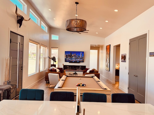 A spacious living room with a pool table, comfortable seating, a television, and a cityscape view.