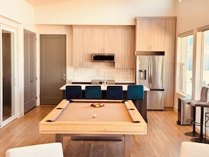 Une cuisine moderne avec des meubles en bois, un réfrigérateur en acier inoxydable et une table de billard.
