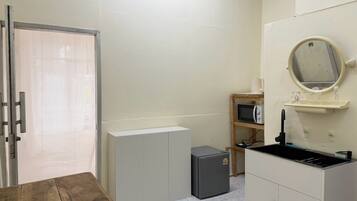A compact kitchenette with a microwave, a small refrigerator, and a sink with a mirror above it.
