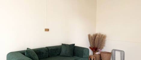 A green sofa in a room with a white wall, a wooden floor, and a small wooden stool.