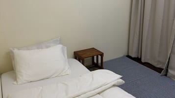 A single bed with white bedding, a small wooden nightstand, and a window with white curtains.
