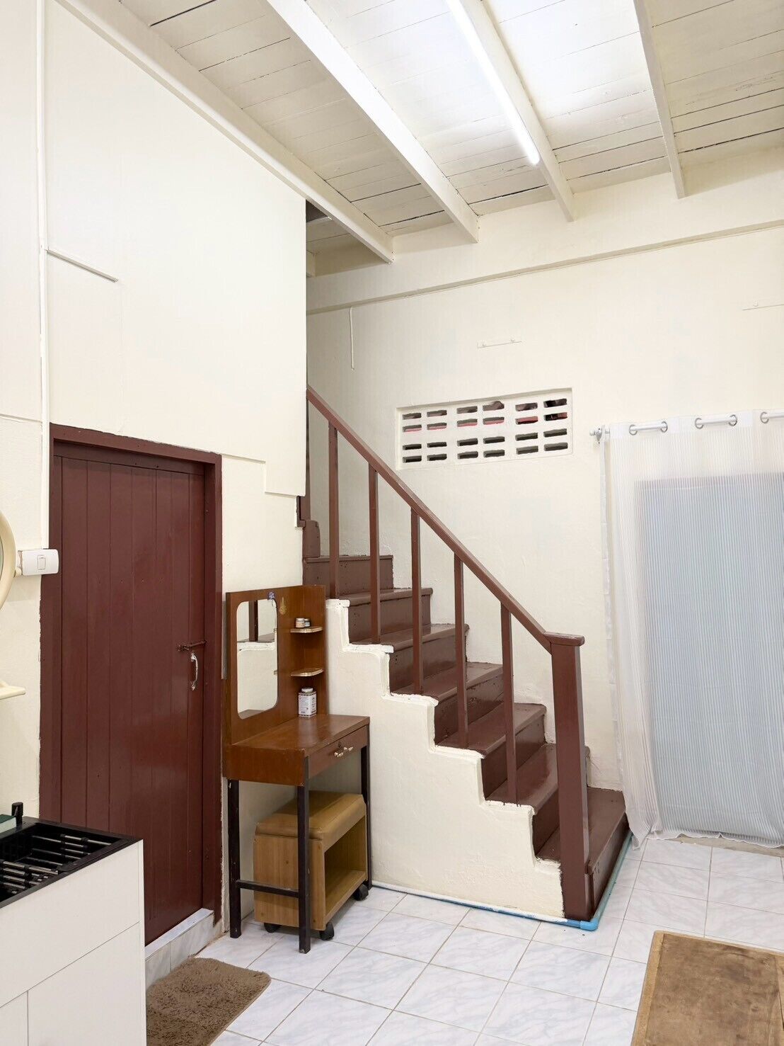 A staircase with wooden steps and a handrail, a brown door, and a white wall with a small window.