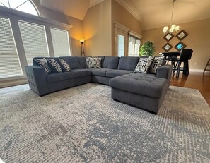 A living room with a sectional sofa, ottoman, and patterned rug.