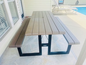 Een picknicktafel met een bank aan weerszijden, geplaatst op een terras met een zwembad op de achtergrond.