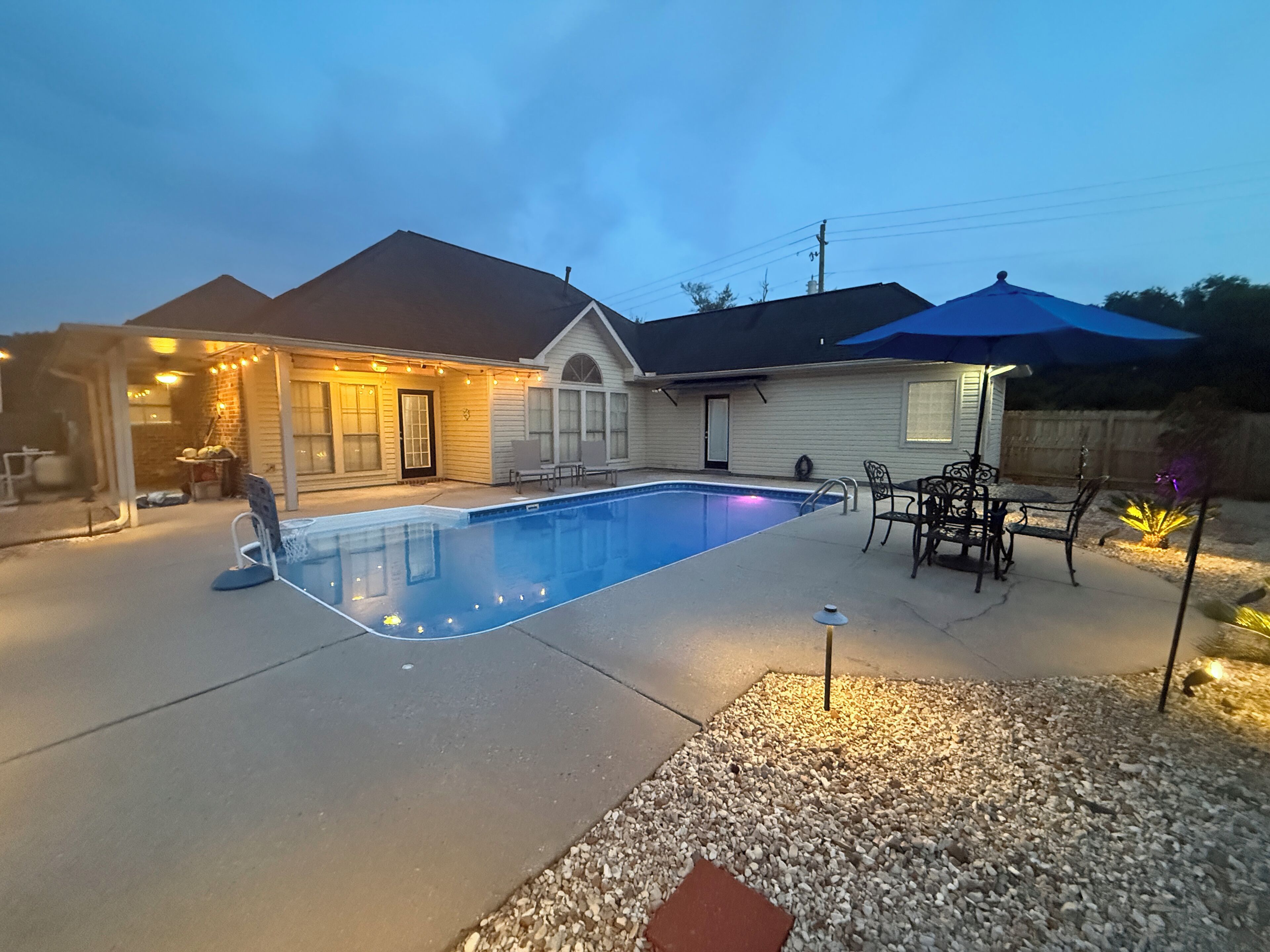 A residential backyard with a swimming pool, patio furniture, and a covered seating area.