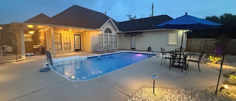 A residential backyard with a swimming pool, patio furniture, and a covered seating area.