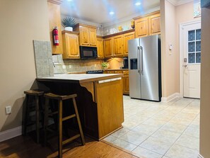 A kitchen with wooden cabinets, a stainless steel refrigerator, and a bar stool.