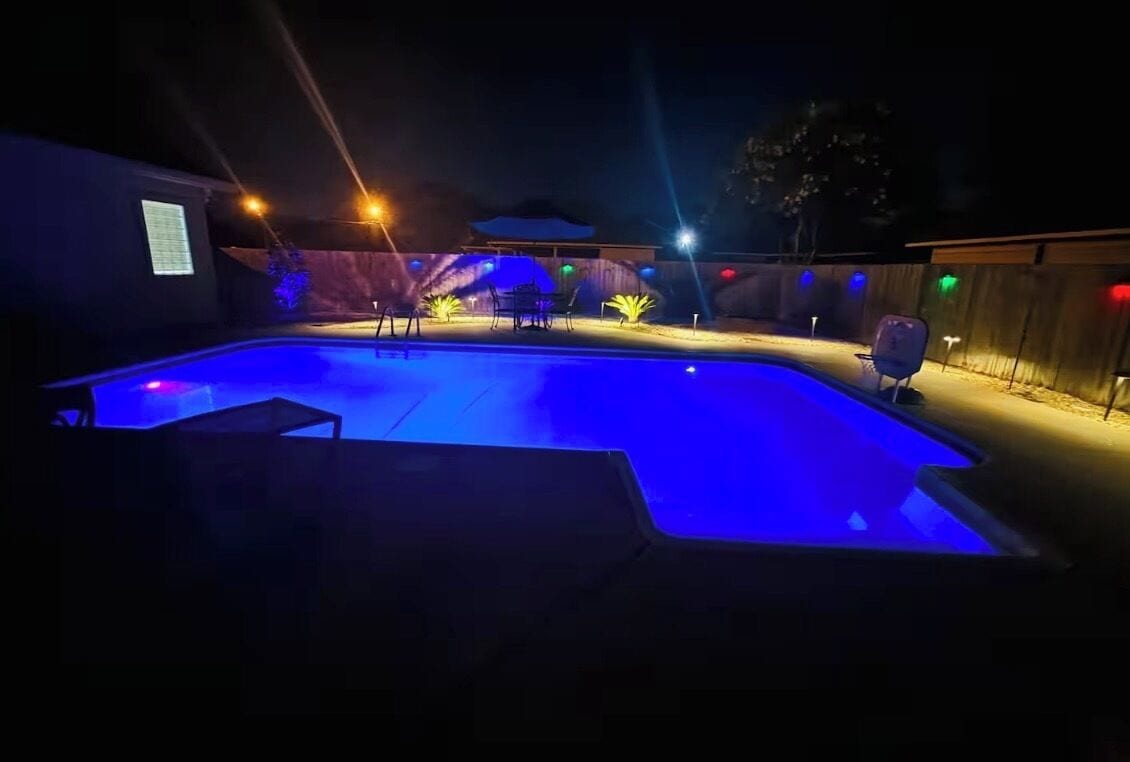 A swimming pool area with a curved edge, surrounded by a wooden fence and illuminated by colorful lights.