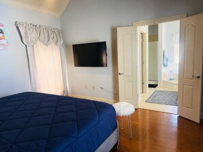 A bedroom with a bed, a television mounted on the wall, and a door leading to a bathroom.