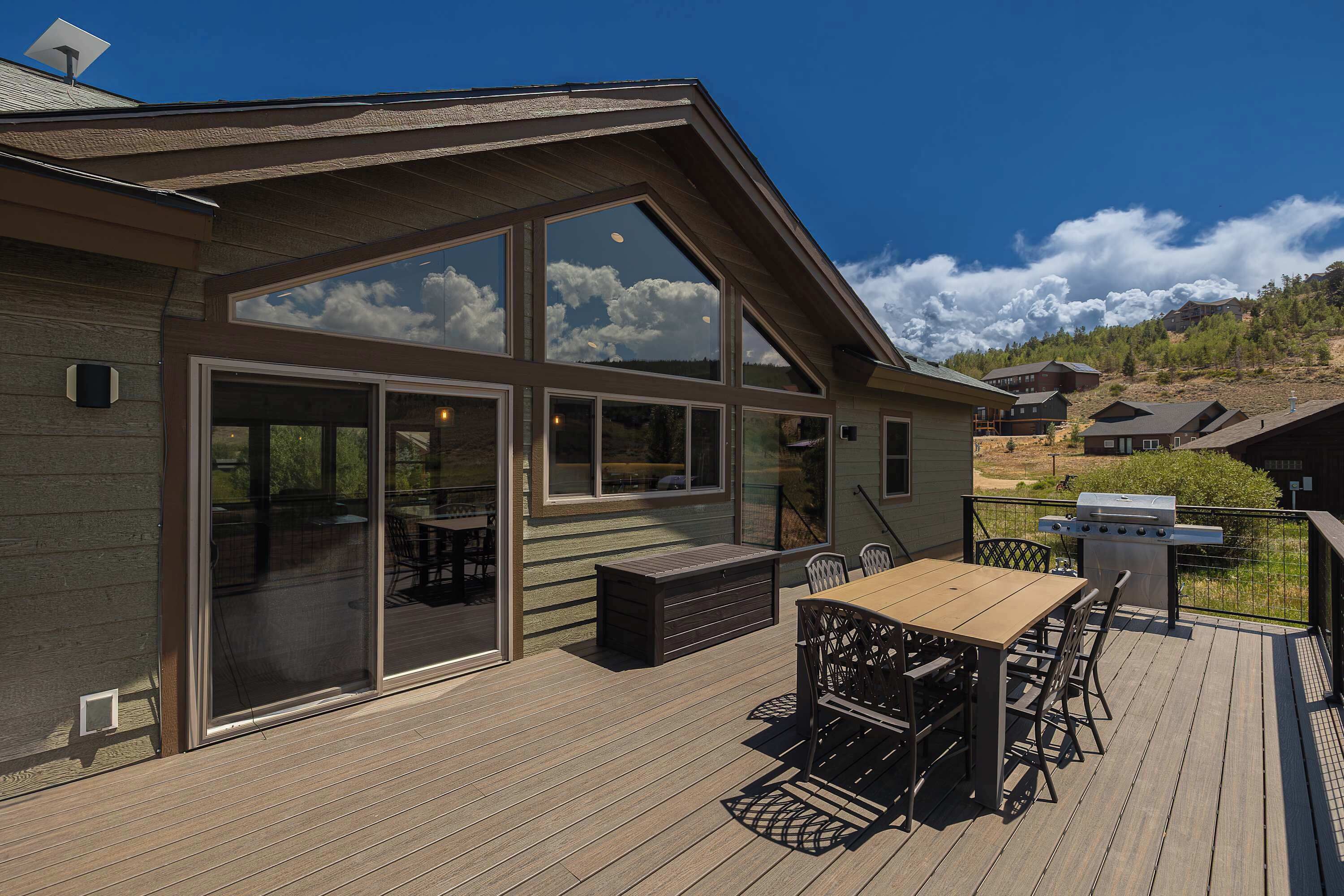 A modern house with a large deck, a barbecue grill, and a scenic mountain view.
