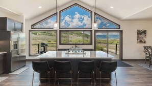 A spacious kitchen with a large island, bar stools, and a view of a mountainous landscape through large windows. - Mountain Retreat at the Base of Granby Ranch (Granby)
