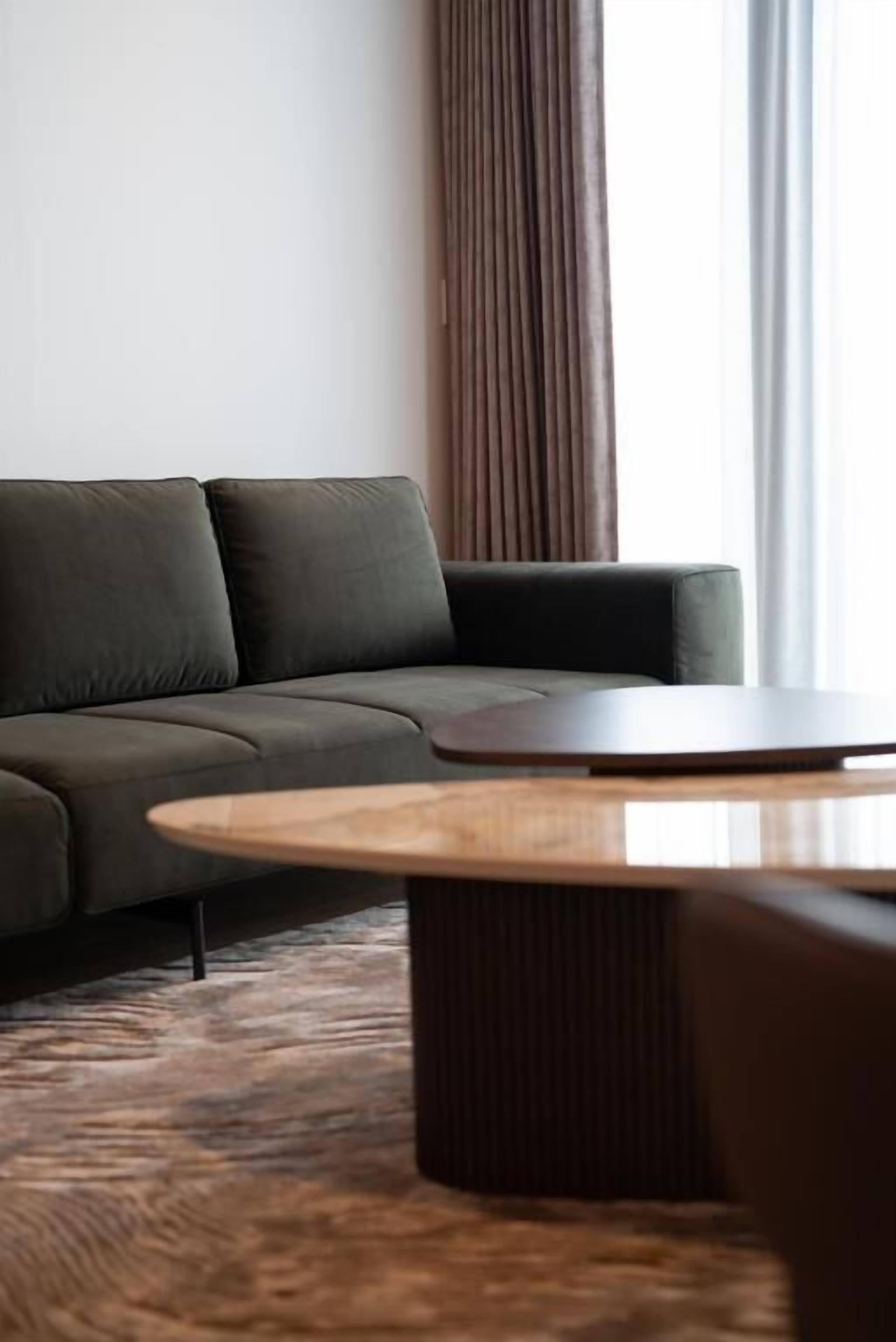 Een moderne woonkamer met een donkergroene bank, een ronde houten salontafel en een kamerbreed tapijt met een patroon.