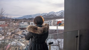 A person in a fur-lined coat looking out over a snowy landscape with mountains in the distance.