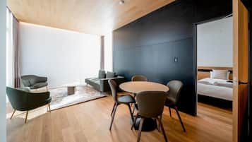 Une chambre d’hôtel moderne avec un plafond en bois, un mur d’accent de couleur foncée, une table à manger ronde avec des chaises, un canapé et un lit doté d’une tête de lit blanche.