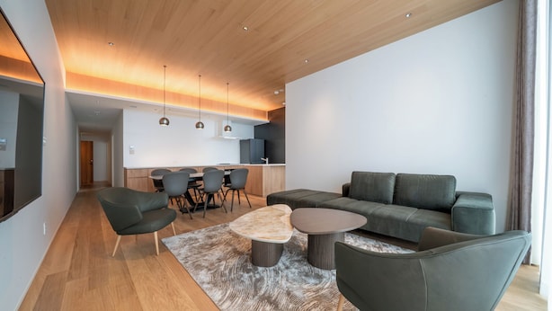 Una sala de estar moderna con un sofá, sillas, una mesa de centro y una cocina al fondo.
