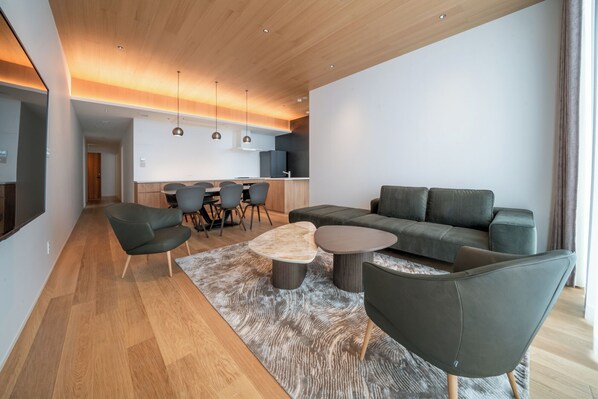 A modern living room with a sofa, chairs, a coffee table, and a kitchen in the background.