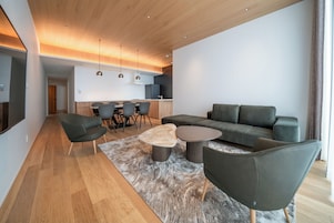 Una sala de estar moderna con un sofá, sillas, una mesa de centro y una cocina al fondo.