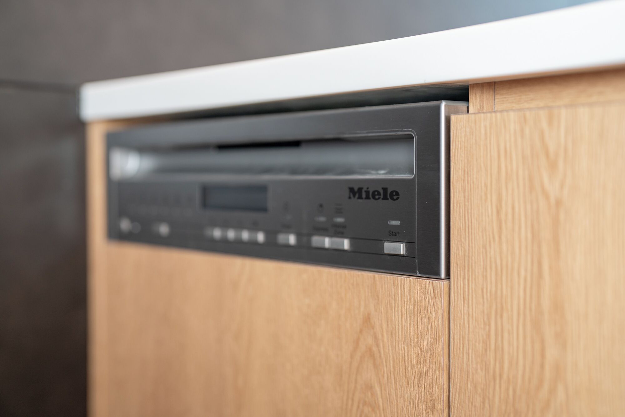A black dishwasher with the brand name 'Miele' on a wooden cabinet.