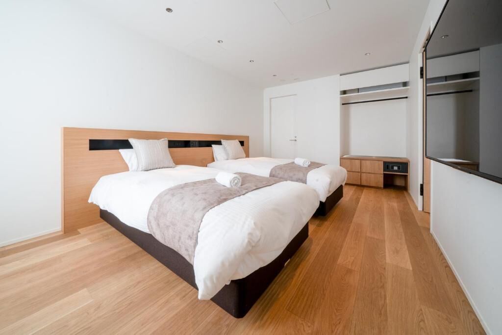 Quarto de hotel com duas camas, um guarda-roupa e uma pequena escrivaninha.