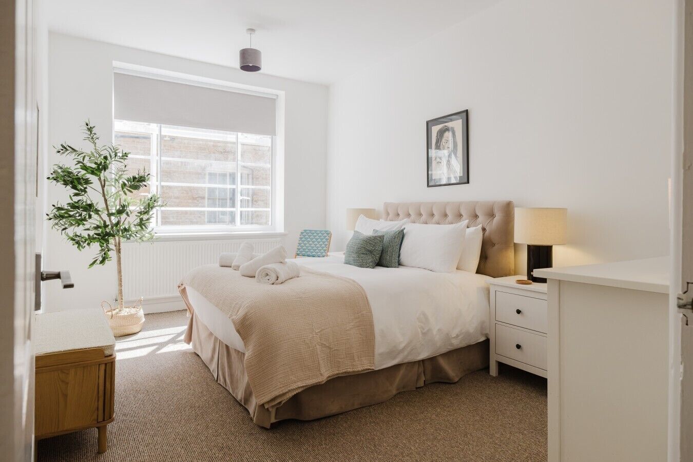 A bedroom with a bed, bedside tables, a lamp, a potted plant, and a window.