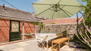 A patio with a table and chairs, a large umbrella, and a stone wall. - Beautiful Cottage in the Heart of Malmesbury (Malmesbury)