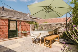 A patio with a table and chairs, a large umbrella, and a stone wall. - Beautiful Cottage in the Heart of Malmesbury (Malmesbury)