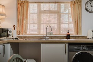 A kitchen with a sink, a washing machine, a clock, and a window with curtains. - Beautiful Cottage in the Heart of Malmesbury (Malmesbury)