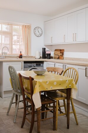A compact kitchen with a dining table, chairs, a clock, and a coffee maker. - Beautiful Cottage in the Heart of Malmesbury (Malmesbury)