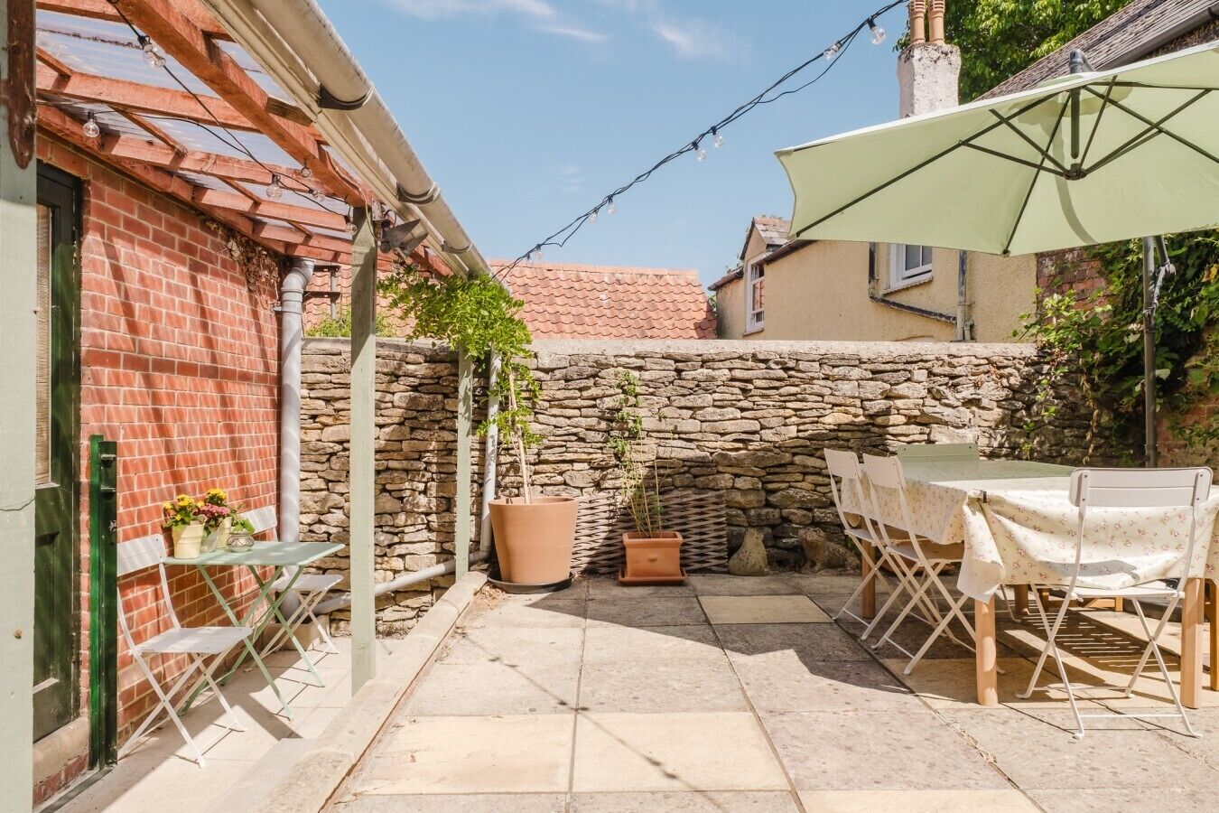 A patio area with a table and chairs, a stone wall, and a hanging light fixture.