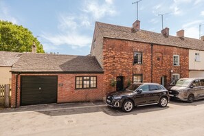 A two-story brick house with a garage, a driveway, and two parked cars.