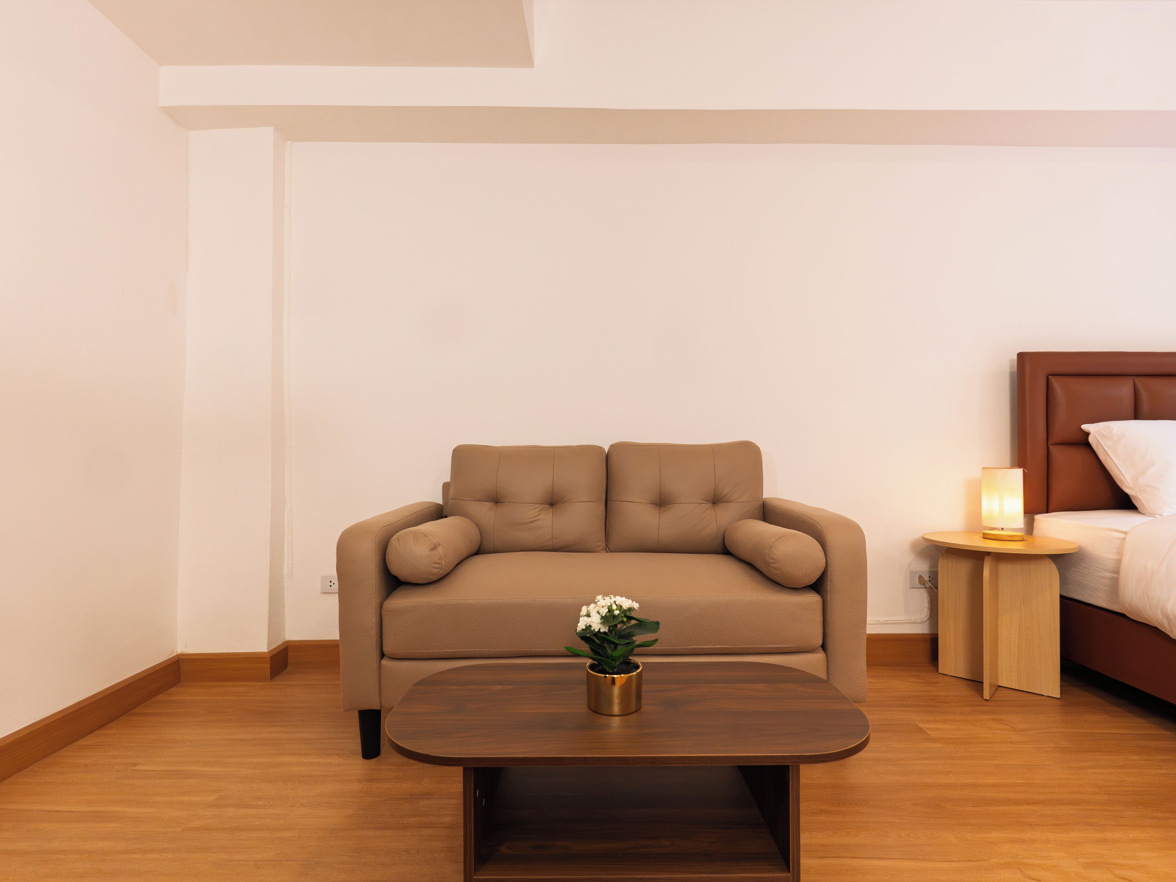Un canapé aux couleurs neutres agrémenté d’un coussin, une table basse en bois avec une plante, et une table de chevet avec une lampe.
