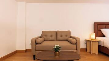 Un canapé aux couleurs neutres agrémenté d’un coussin, une table basse en bois avec une plante, et une table de chevet avec une lampe.