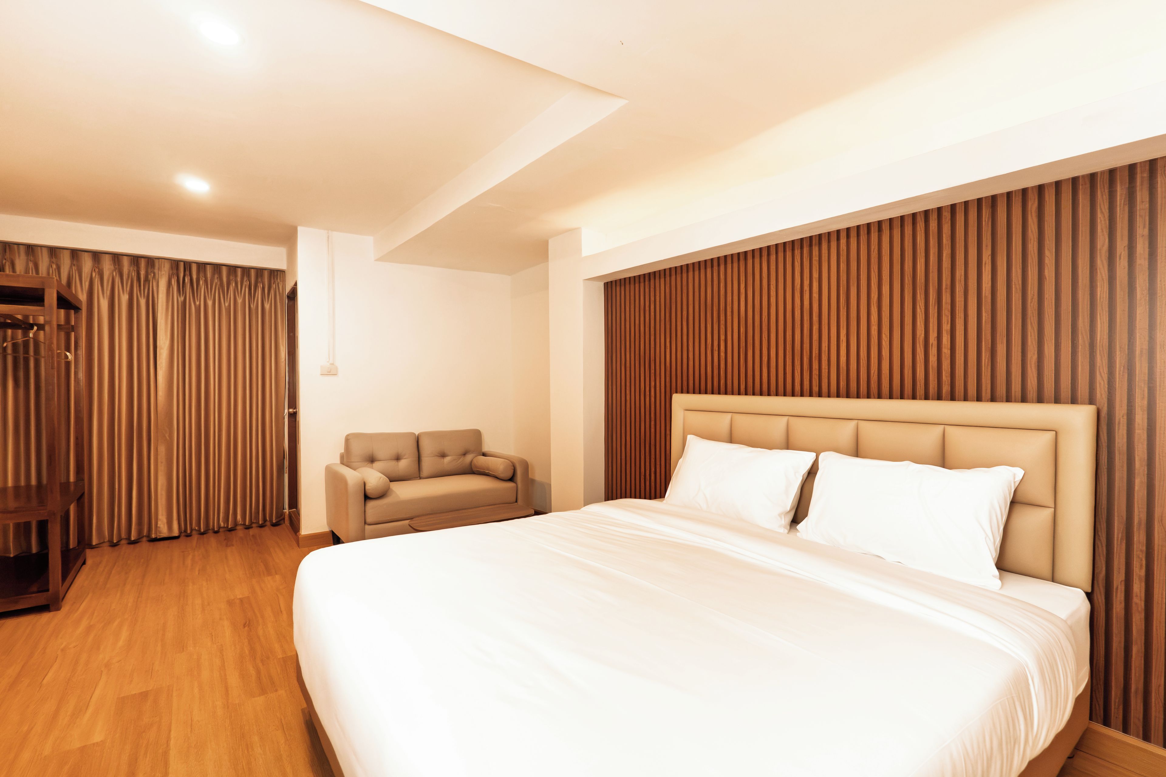 A modern hotel room with a large bed, a seating area, and a wooden panel wall.