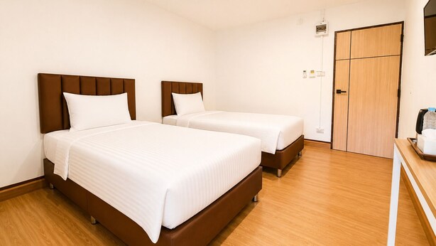 Quarto de hotel com duas camas, um guarda-roupa de madeira e uma mesa com uma garrafa de água.