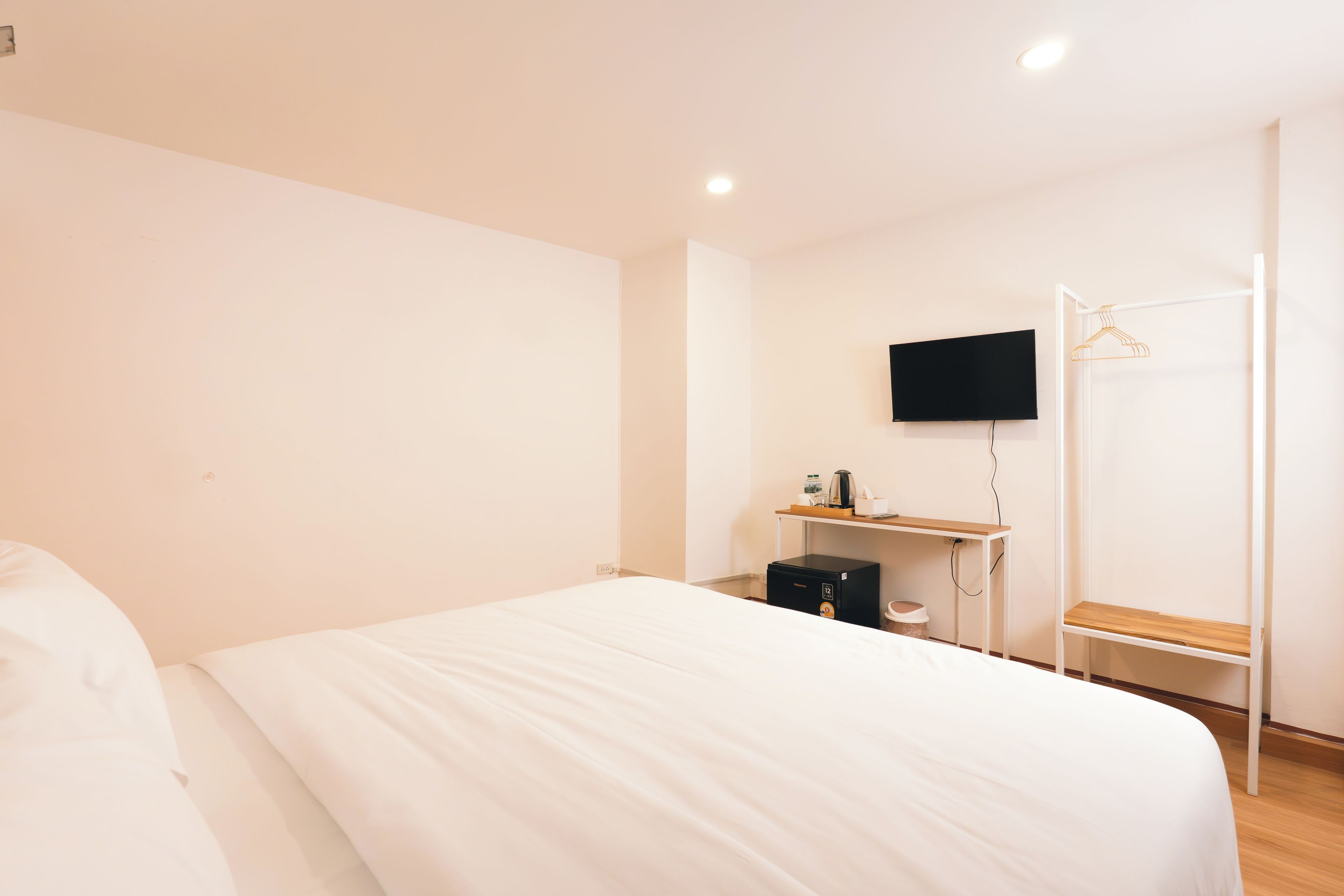Quarto de hotel com cama, escrivaninha, televisão de tela plana, cafeteira e cabideiro.