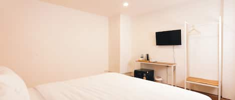 A hotel room with a bed, a desk with a flat-screen TV, a coffee maker, and a coat rack.