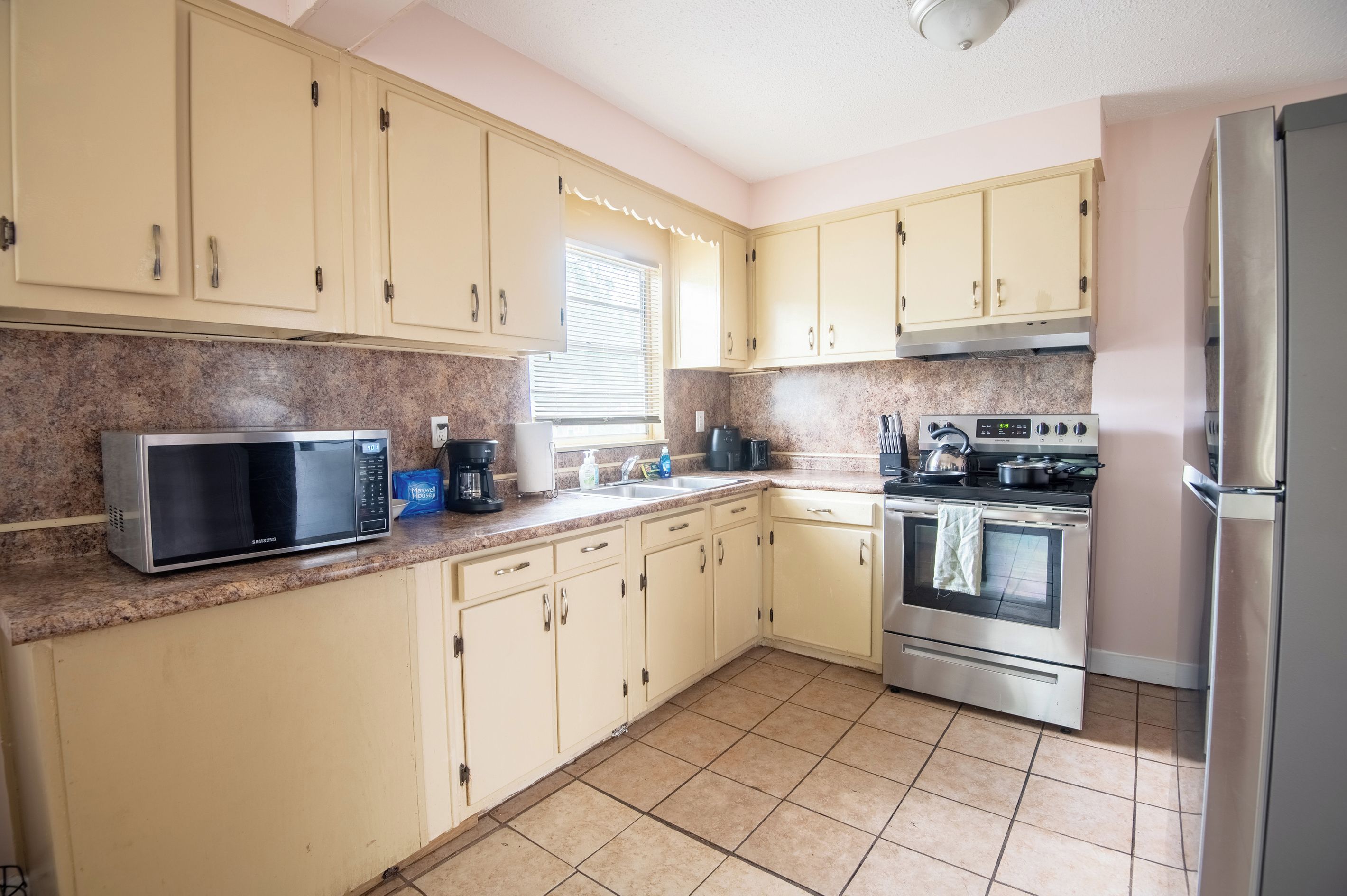 A kitchen with light-colored cabinets, a stainless steel microwave, a stove, and a refrigerator.