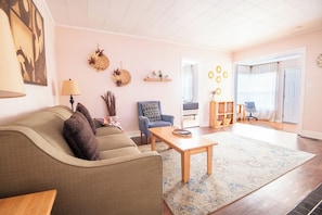 A living room with a sofa, armchair, coffee table, and a view into another room through an open door.